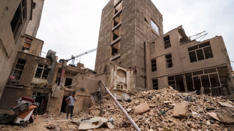 An Iranian man speaks on his mobile phone as he stands on the debris in front of destroyed buildings following a military strike on Tehran, Iran, on March 15, 2026. (Atta KENARE / AFP via Getty Images)
